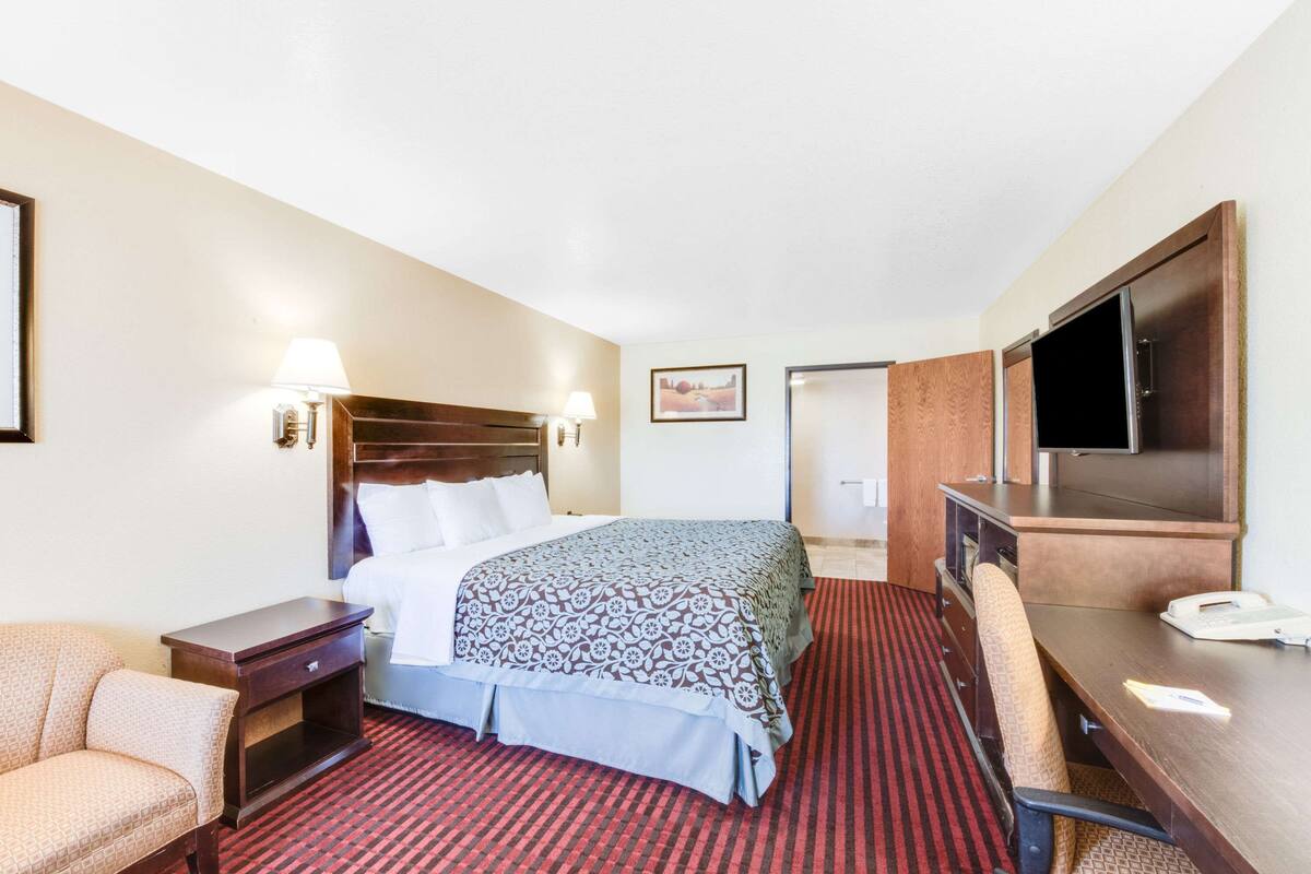 A hotel room with a bed, a desk with a chair, a TV, and a lamp.
