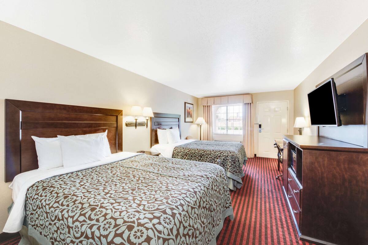 A hotel room with two beds, a TV, a dresser, and a window with curtains.