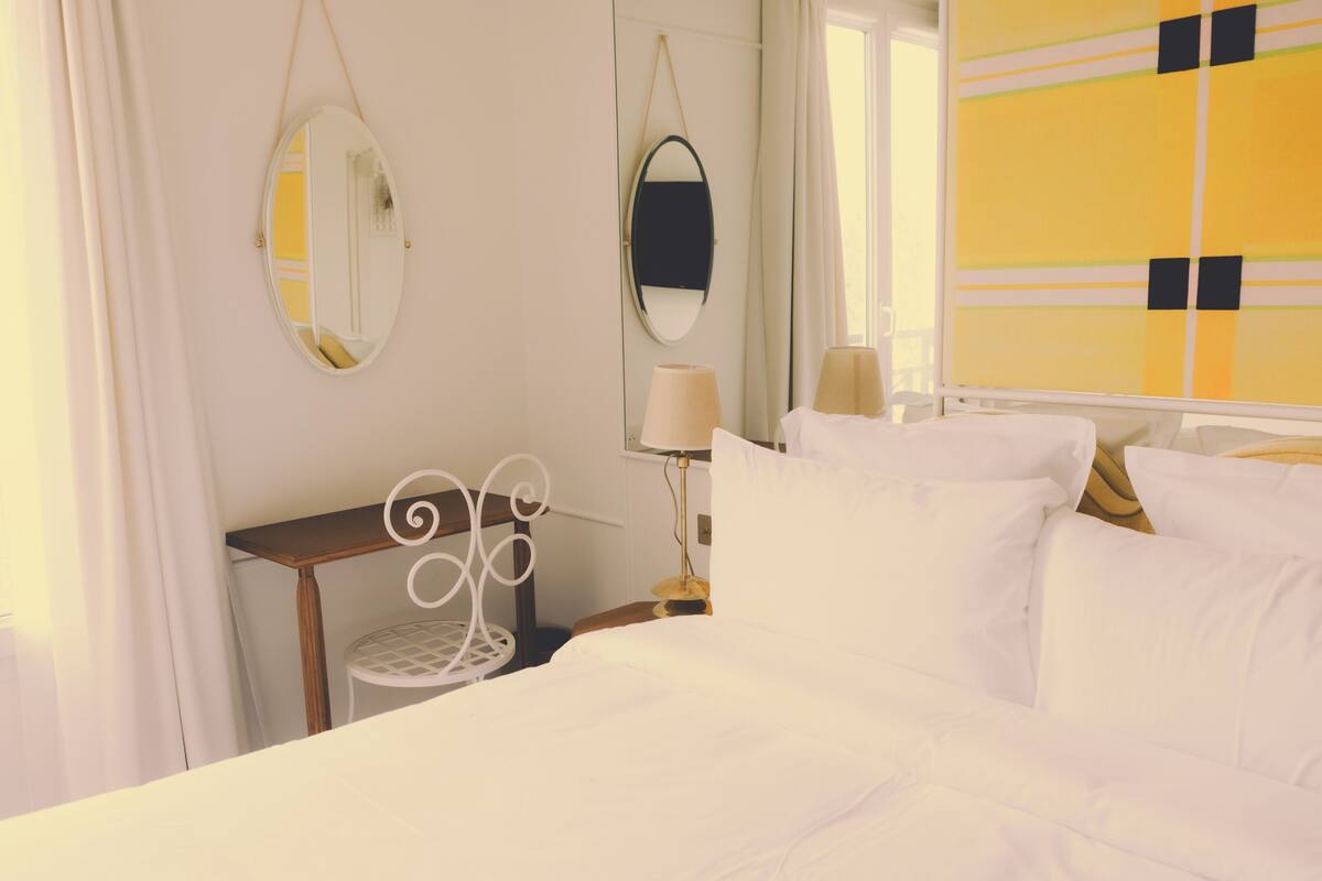 A hotel room with a bed, two bedside tables, a mirror, and a window with curtains.