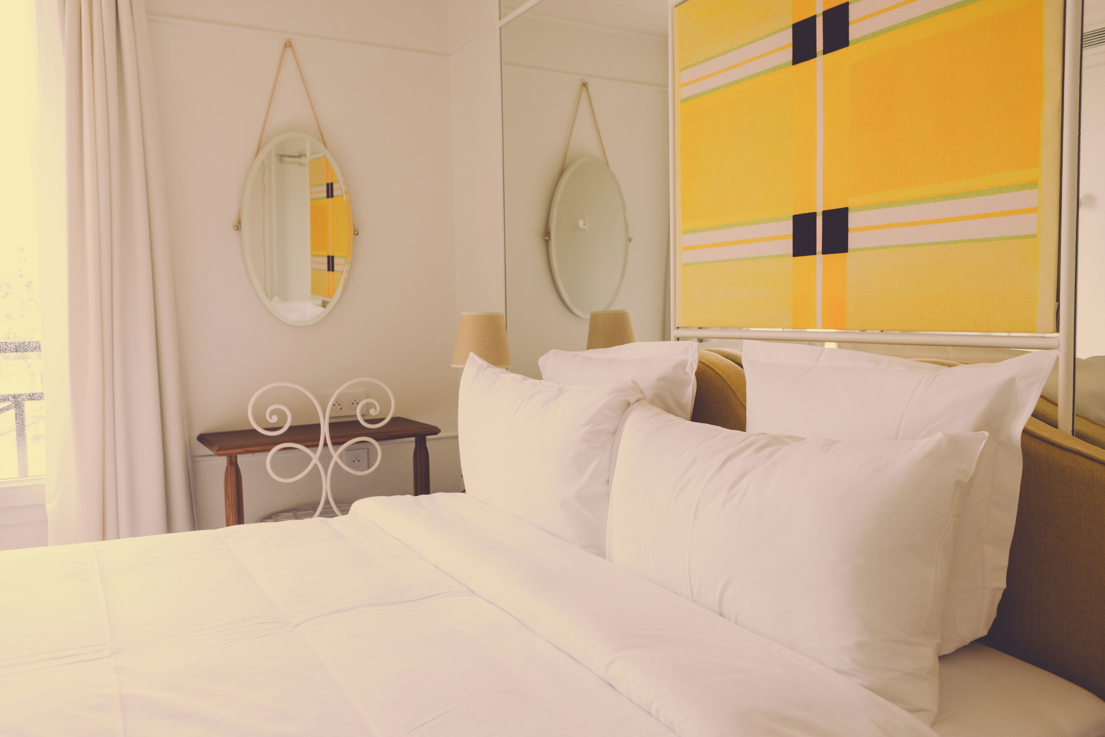 Una habitación de hotel con cama, dos mesitas de noche, un espejo y una ventana con cortinas.