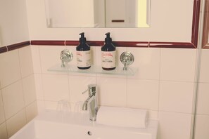 Ett badrum med ett vitt handfat, två svarta flaskor med hudvårdsprodukter och en spegel ovanför handfatet.