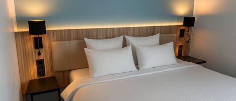 Una habitación de hotel con una cama grande, dos mesitas de noche y lámparas fijadas a la pared.