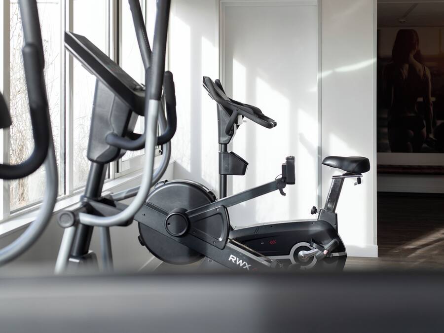 Una bicicleta estática en una habitación con un ventanal grande, un banco y un espejo montado en la pared.