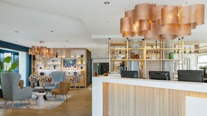 Un espace d’accueil moderne avec un bureau en bois, un grand luminaire suspendu et un coin salon comprenant des fauteuils et un tapis.