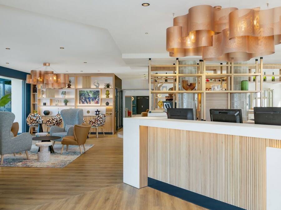 Uma área de recepção moderna com uma mesa de madeira, uma luminária pendente grande e um espaço de estar com cadeiras e um tapete.