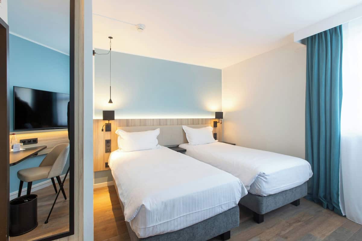Une chambre d’hôtel avec deux lits, un bureau, une chaise et un téléviseur.