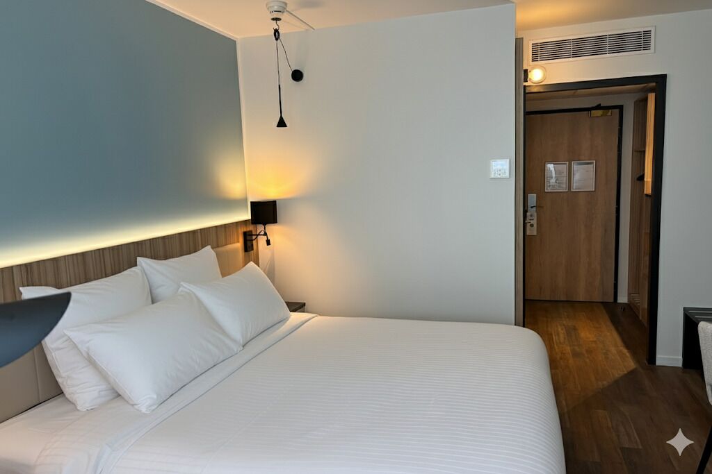 A hotel room with a large bed, a bedside lamp, and a door leading to a hallway.
