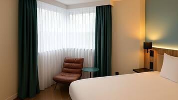 Una camera d'albergo con un letto, una sedia, un tavolino e una finestra con tende.