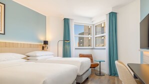 Une chambre d’hôtel avec deux lits, un bureau, une chaise, une télévision et une fenêtre avec des rideaux.
