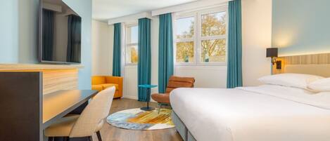 Une chambre d’hôtel avec un lit, un bureau, une chaise, une télévision et une fenêtre avec des rideaux.