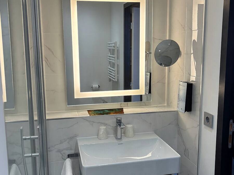Une salle de bain moderne avec une douche à parois de verre, un lavabo blanc avec un miroir au-dessus et un porte-serviettes.