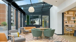 Un intérieur moderne avec un sol à motifs géométriques, un coin salon avec des canapés et des fauteuils, une table ronde en bois et un tabouret noir décoratif.