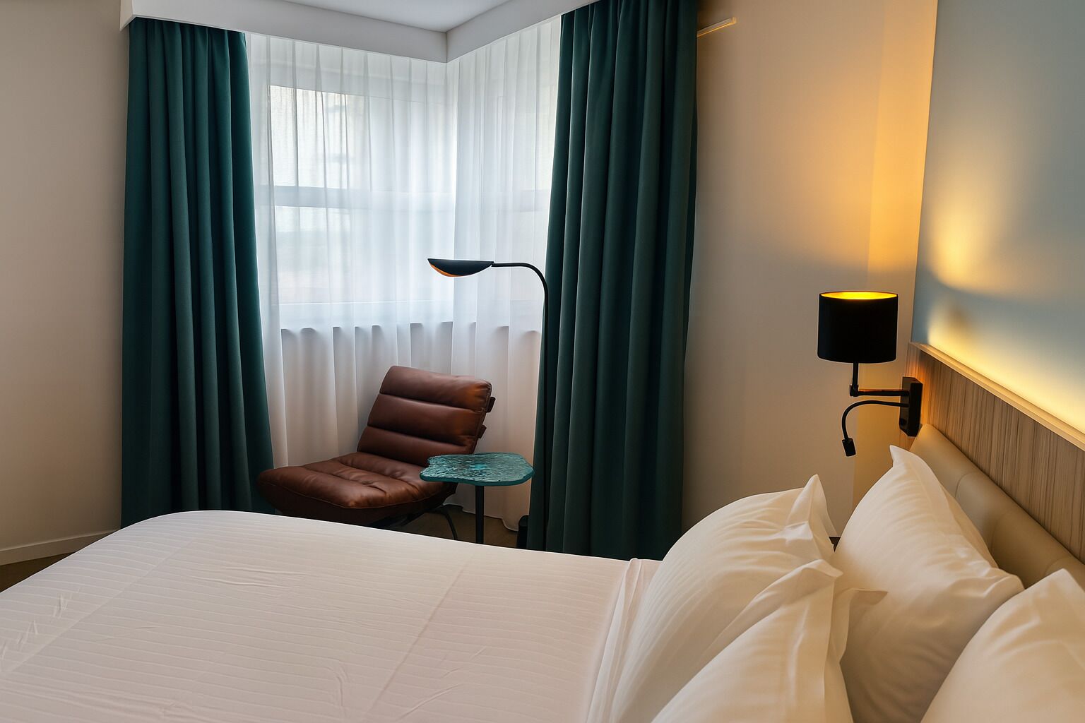 A hotel room with a bed, a chair, a small table, and a lamp.