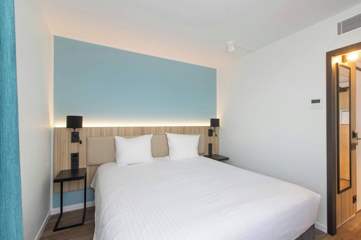 Une chambre d’hôtel avec un grand lit, des tables de chevet, une lampe fixée au mur et une porte dotée d’un miroir.