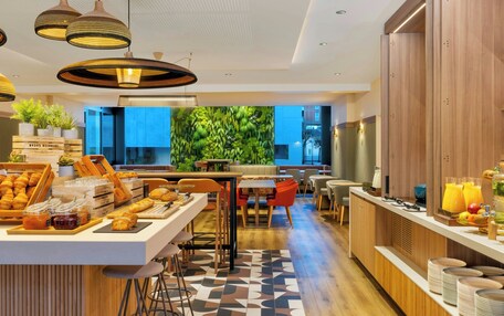 A modern hotel lobby with a central seating area, a buffet with pastries, and a large green wall.