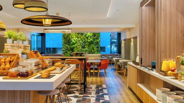 Un hall d’hôtel moderne doté d’un espace salon central, d’un buffet proposant des pâtisseries et d’un grand mur végétal.