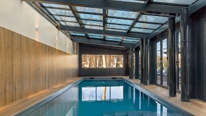 Une piscine intérieure dotée d’un plancher en bois, d’un toit en verre et de grandes fenêtres.