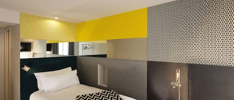 A modern hotel room with a bed, a bedside table, and a mirror.