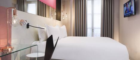 A modern hotel room with a large bed, a glass table, a desk, and a TV on the wall.