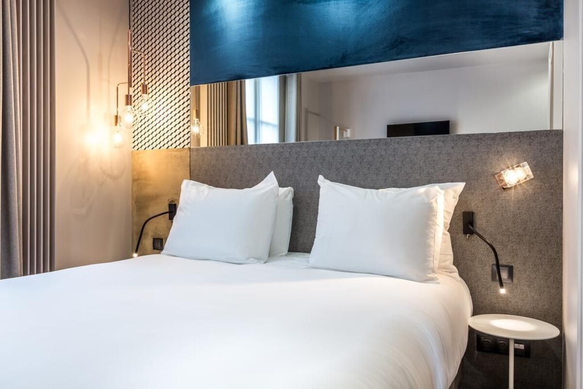 Una habitación de hotel moderna con una cama grande, dos mesitas de noche y un televisor montado en la pared.