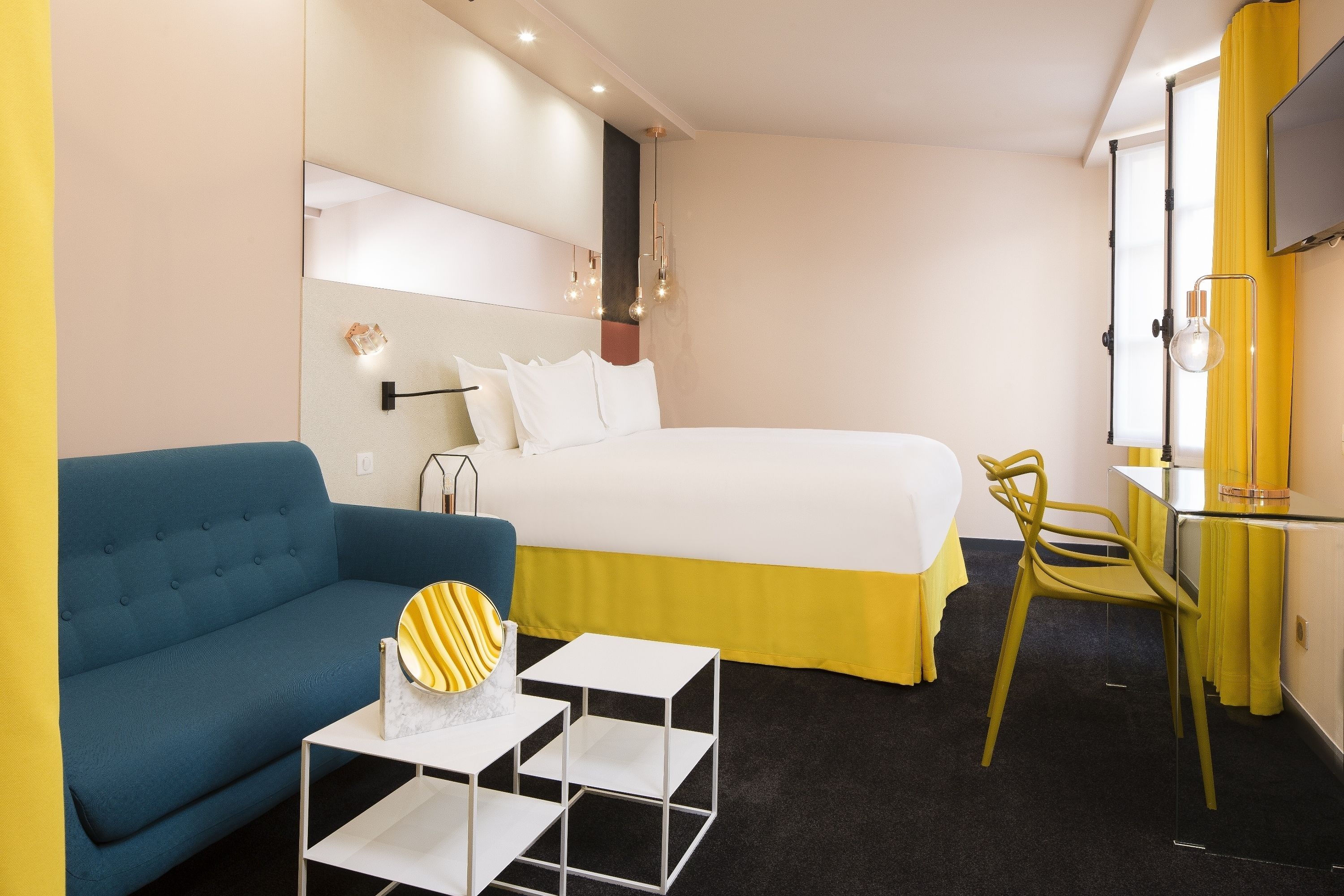 A hotel room with a bed, a blue sofa, a small table, and a chair.