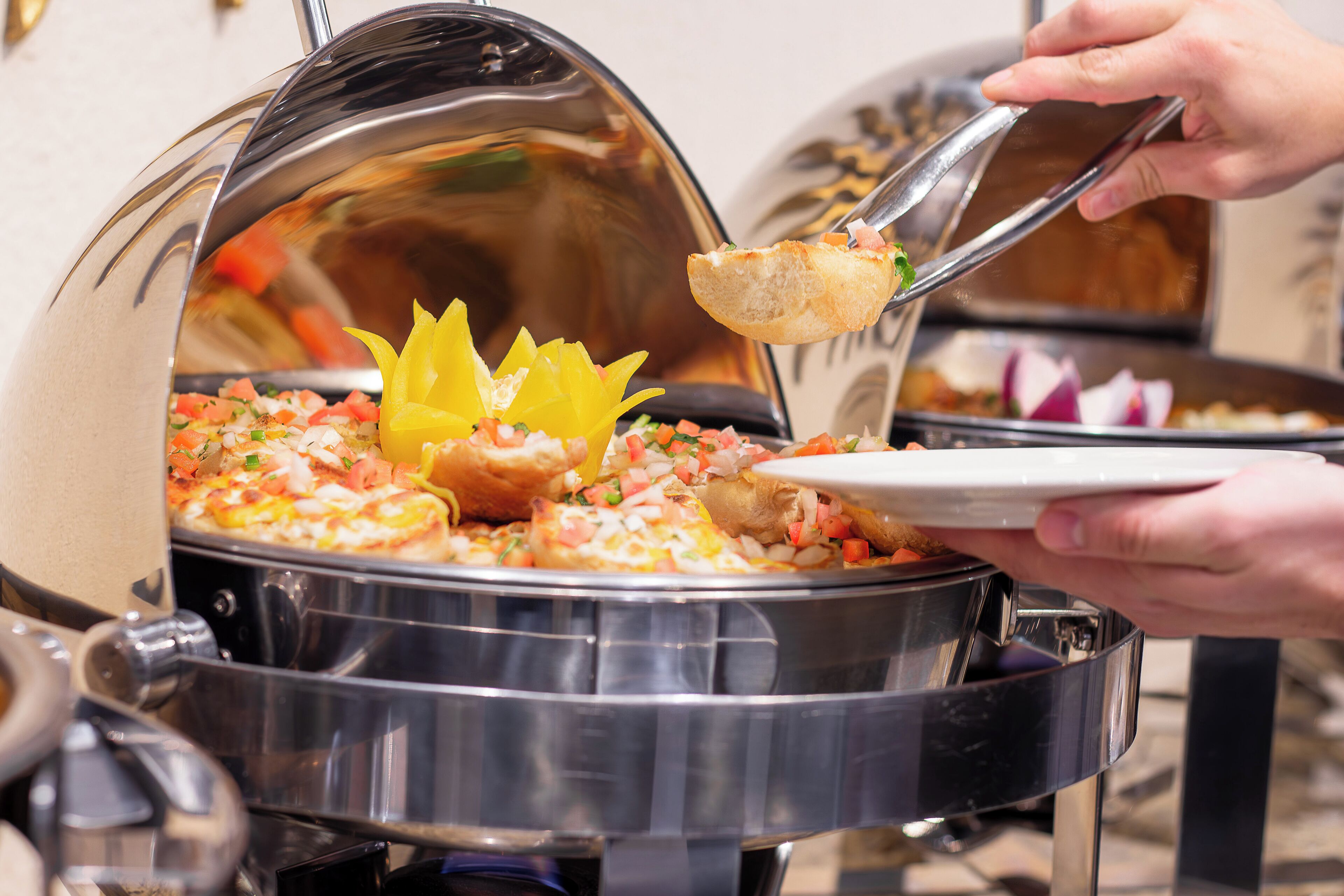 Un'attrezzatura per buffet con diversi piatti, tra cui una grande pentola con il coperchio, un piatto con cibo e una persona che serve con le pinze.