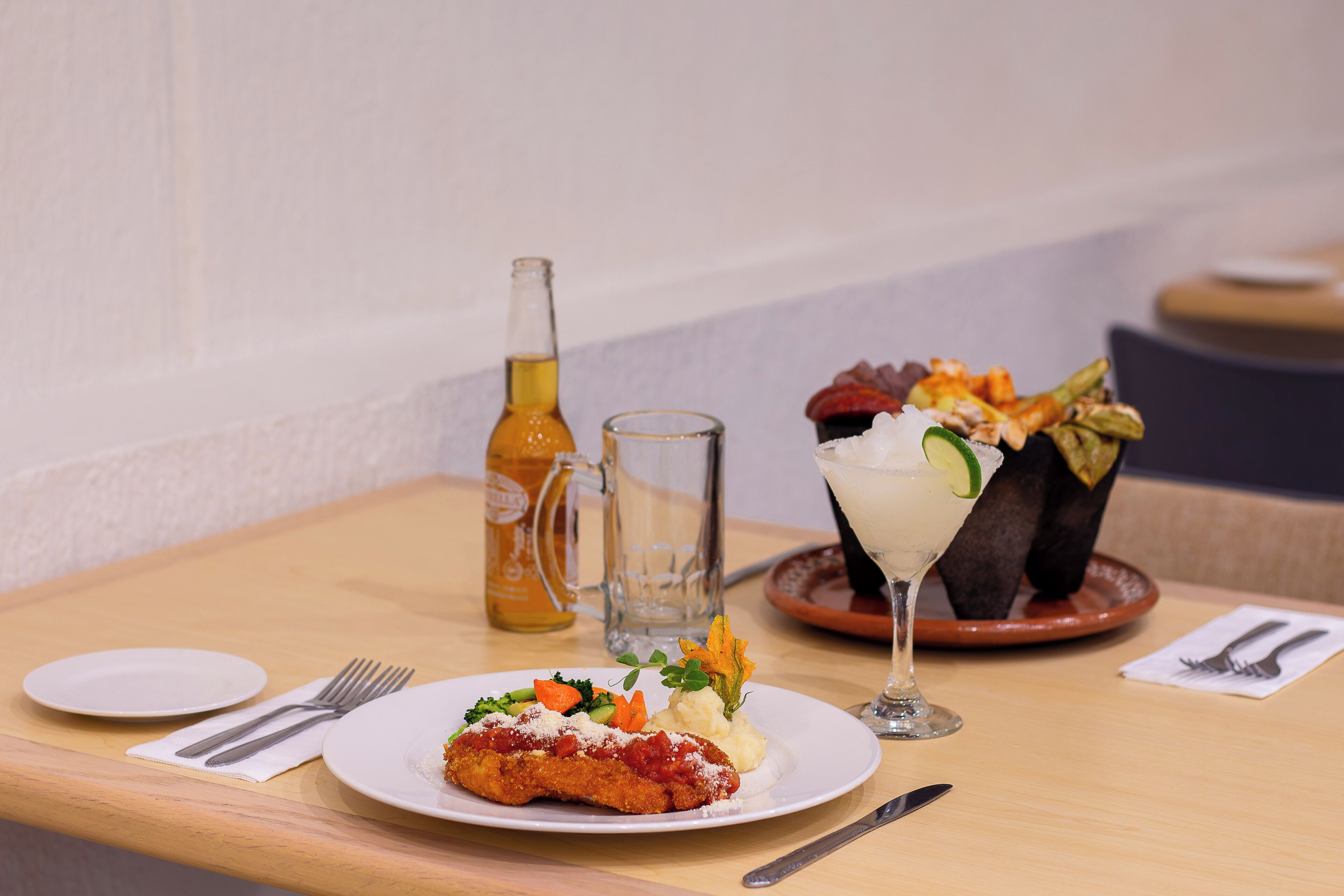 Una mesa de comedor con un plato de comida, un vaso de bebida y una botella.