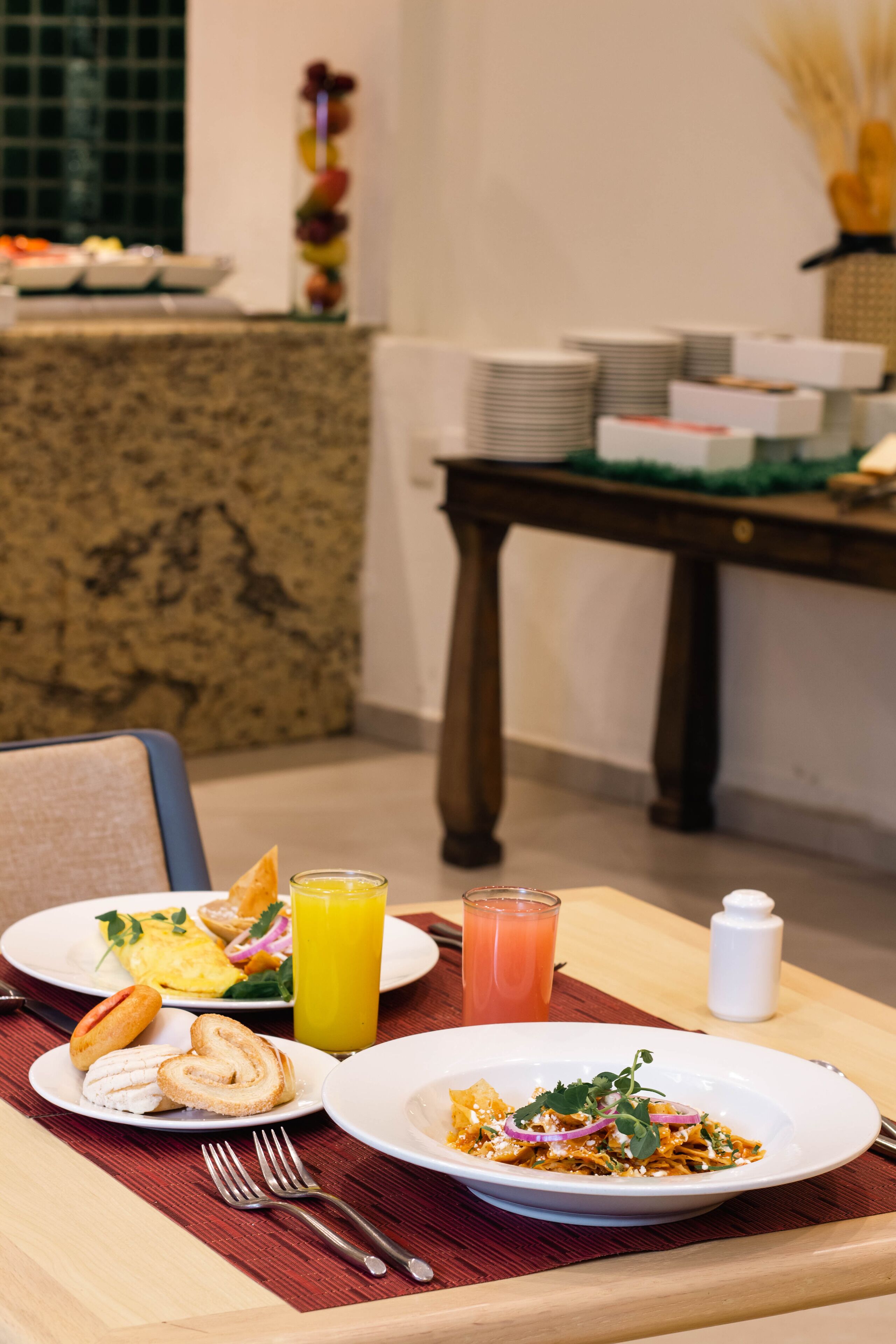 A breakfast table with plates of food, including eggs, toast, and a fruit salad, along with two glasses of orange juice.