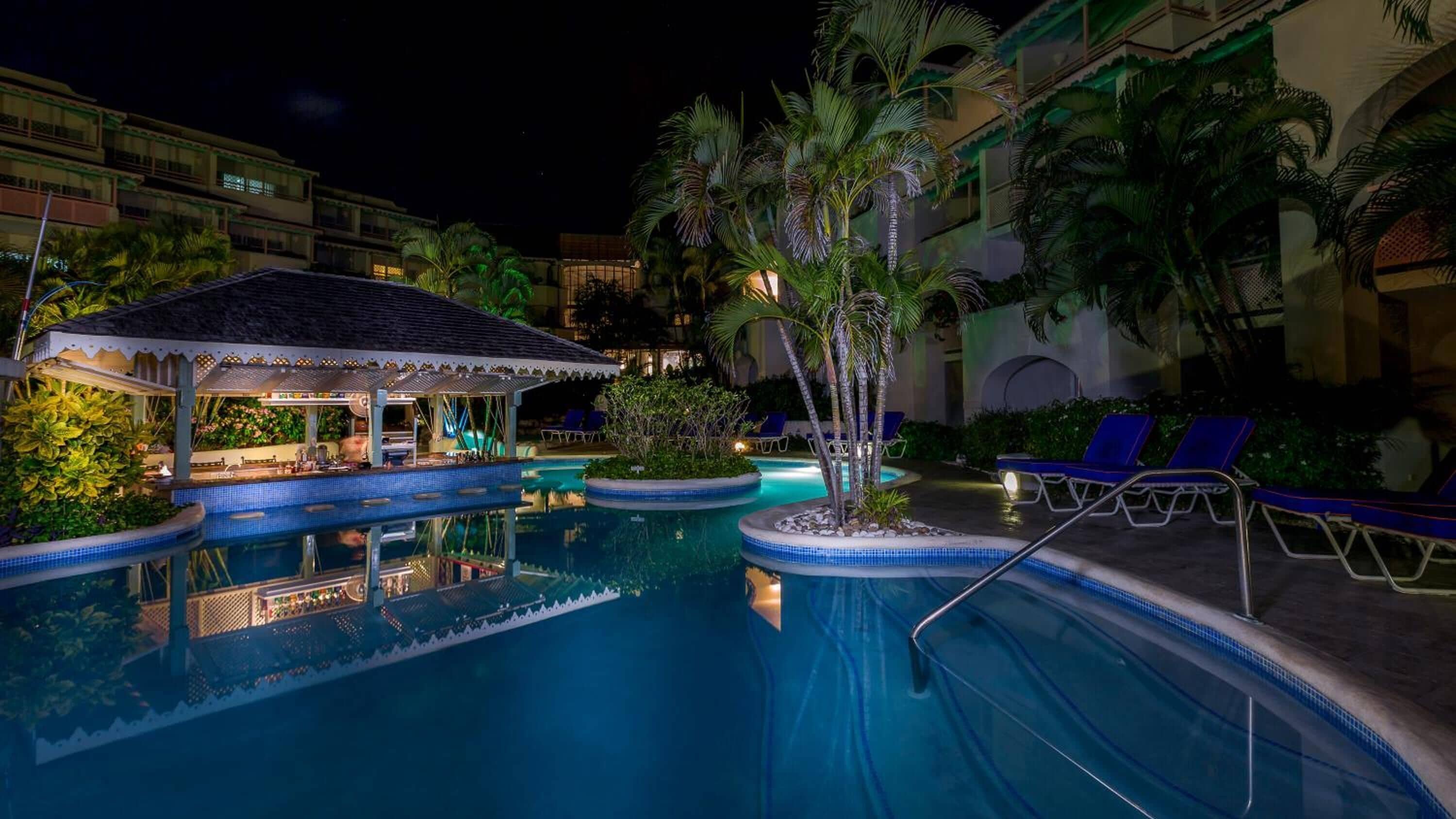 A nighttime pool area with lounge chairs and a bar.