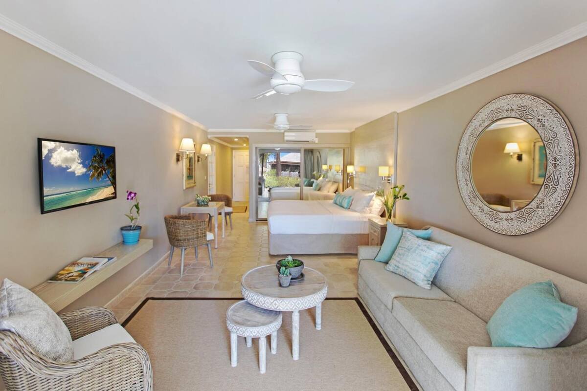A spacious living room with a sofa, a dining table, and a TV mounted on the wall.