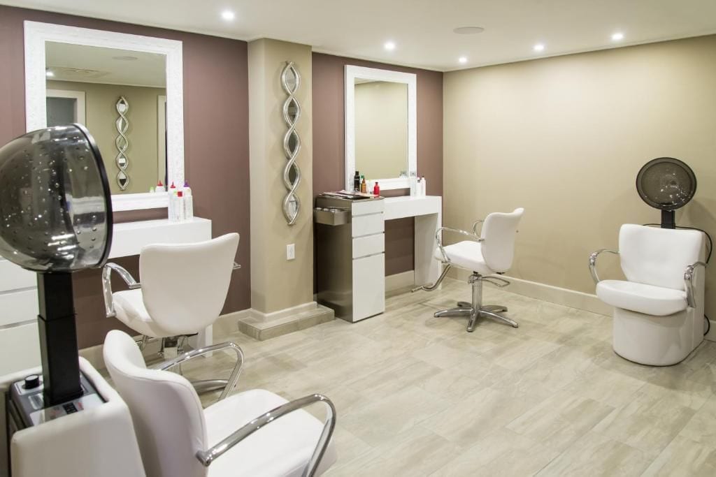 Un baño moderno con tocador, dos sillas blancas, un espejo grande y un secador de pelo.