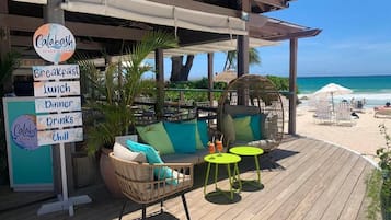 Um restaurante à beira-mar com área externa, incluindo uma cadeira de vime e uma mesa redonda, e um letreiro com opções de refeições.