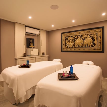 A room with two beds, a mirror, a wall-mounted artwork, and a small kitchenette.