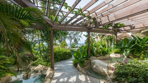 A tropical garden pathway with a pergola, water features, and lush greenery. - Bougainvillea Barbados (Maxwell)