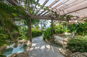 Un percorso in un giardino tropicale con un pergolato, giochi d'acqua e vegetazione lussureggiante.