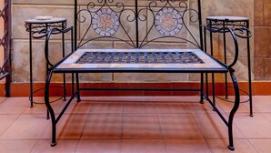 Un banc avec un dossier en mosaïque, situé dans une pièce ornée de colonnes et d’une fresque représentant une statue.