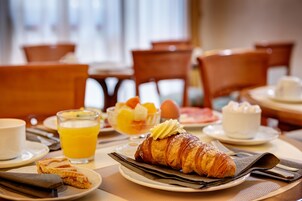 A breakfast setting with croissants, fruit, and orange juice on a table.
