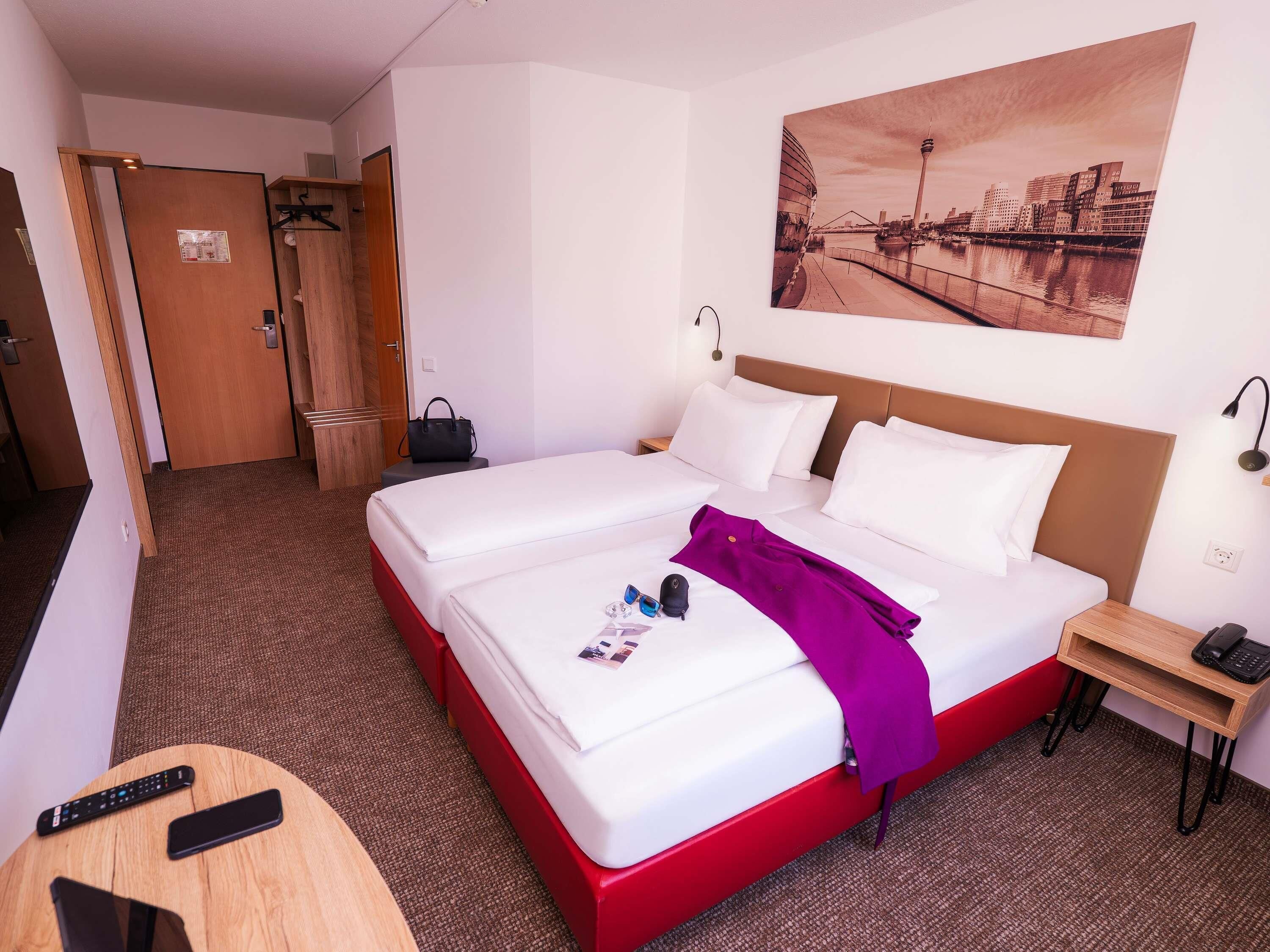 A hotel room with a large bed, two bedside tables, a desk, and a wall-mounted painting.