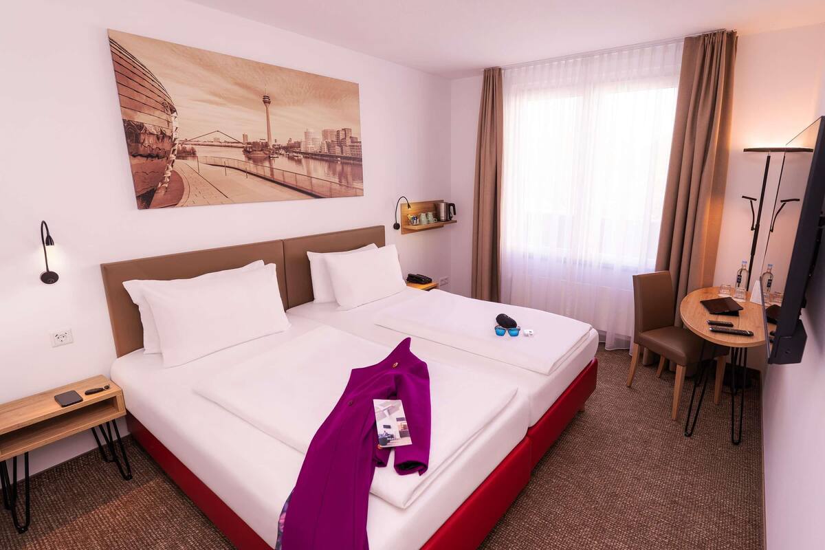 A hotel room with a large bed, a desk, a chair, a television, and a painting on the wall.