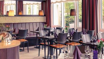 Un restaurante con mesas y cabinas, ventanas amplias y lámparas colgantes.