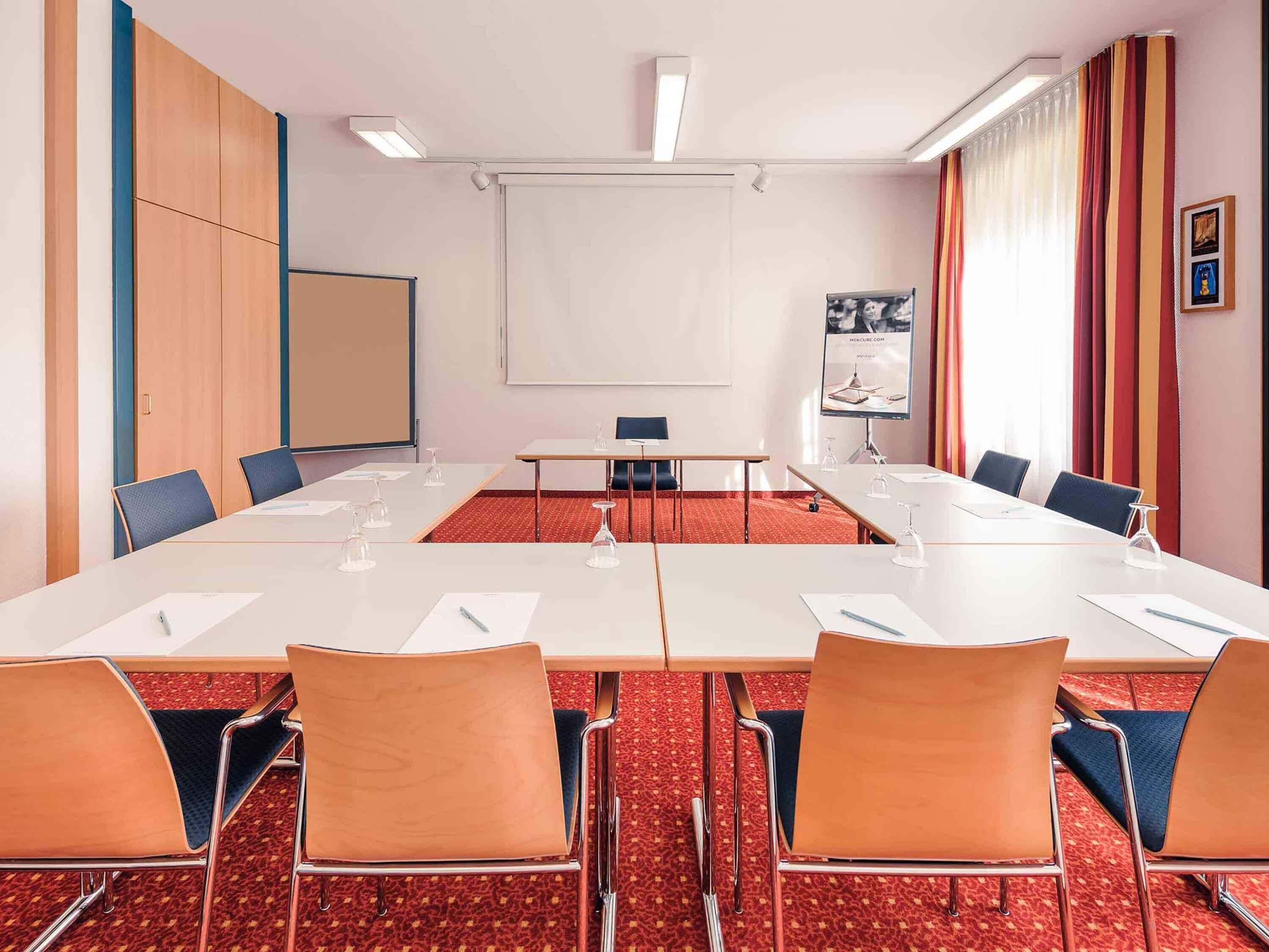 A conference room with a long table, chairs, a projector screen, and a whiteboard.