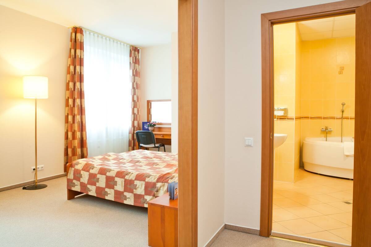 Een hotelkamer met een bed, bureau, stoel, lamp en een badkamer met bad en wastafel.