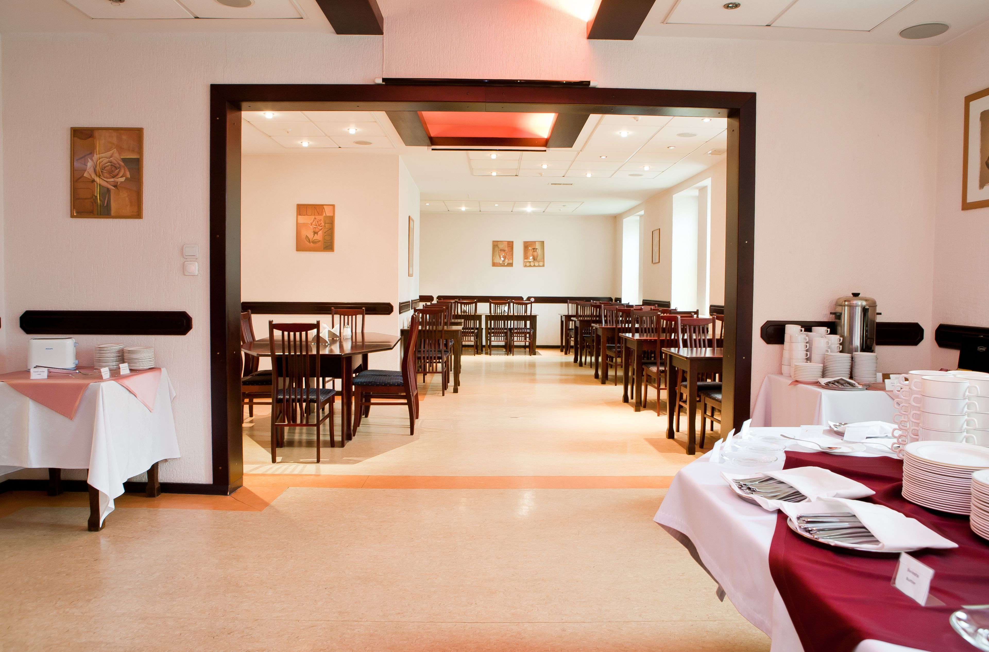 A dining area with multiple tables and chairs, a buffet setup, and a view into another room.