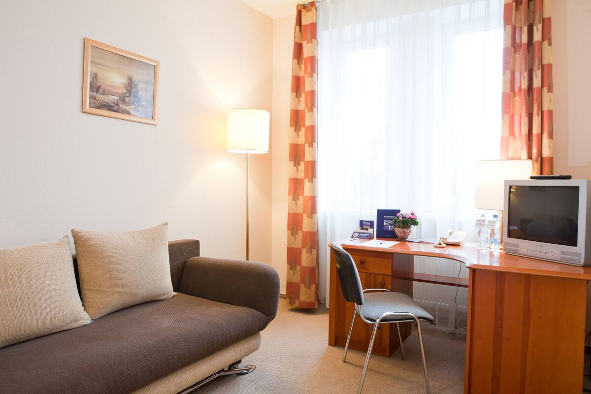 Een hotelkamer met een bank, een bureau met een computer, een televisie en een lamp.