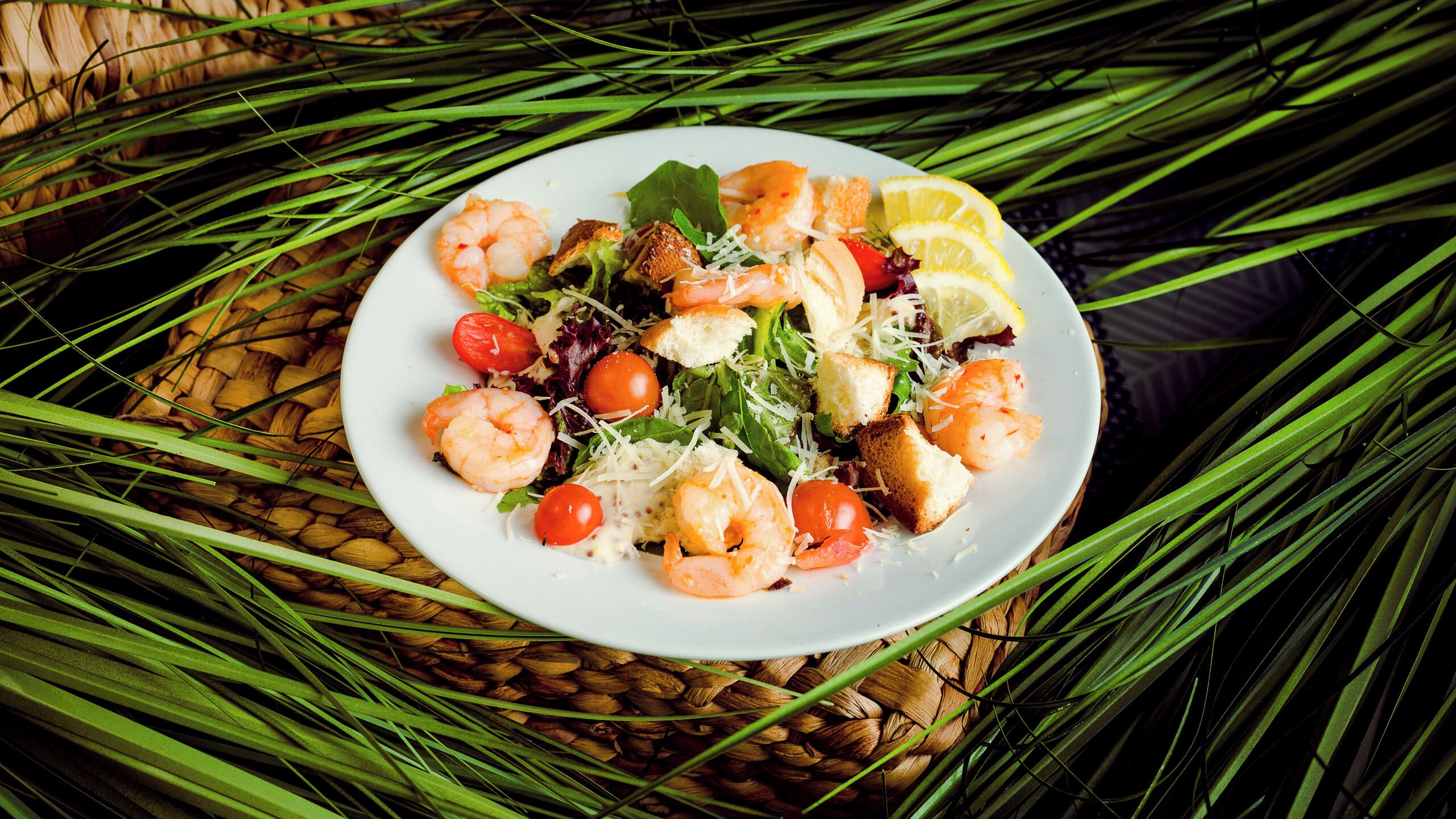 Ensalada de camarones con tomates cherry, lechuga y rodajas de limón, sobre un tapete tejido.
