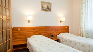 Habitación con dos camas, cabecero de madera, lámparas fijadas a la pared, un cuadro y una ventana con cortinas.