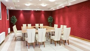 A conference room with a long table and white chairs, red textured walls, and two potted plants.