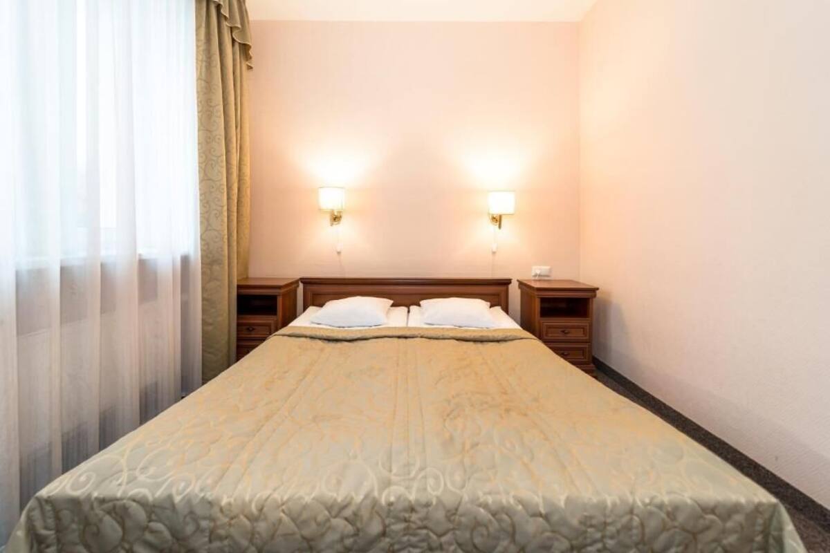 Une chambre d’hôtel avec un grand lit, deux tables de chevet et deux lampes fixées au mur.