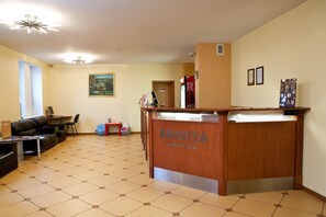 A reception area with a wooden reception desk labeled "BRIGITA HOTEL," a black leather sofa, a small table with a chair, and a painting on the wall. - Kolonna Hotel Brigita (Riga)