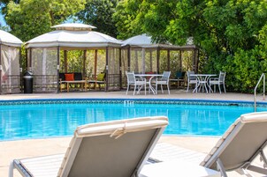 Un área de piscina con sillones, mesas y un pabellón.